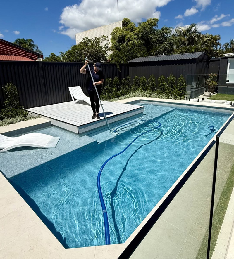 Woman cleaning new pool with dual splash decks and tanning area
